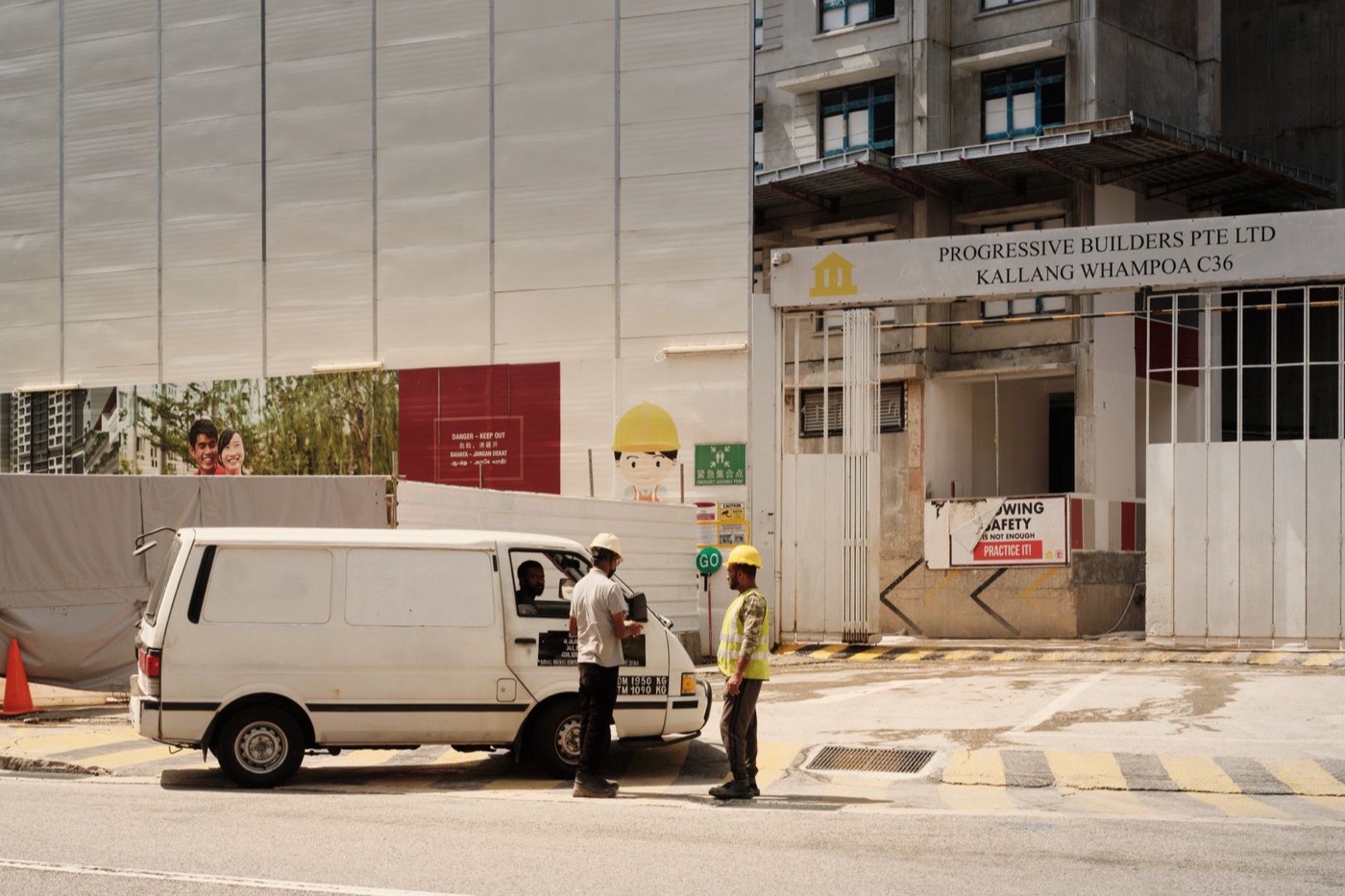Construction workers interacting near a van at a building site in Singapore.