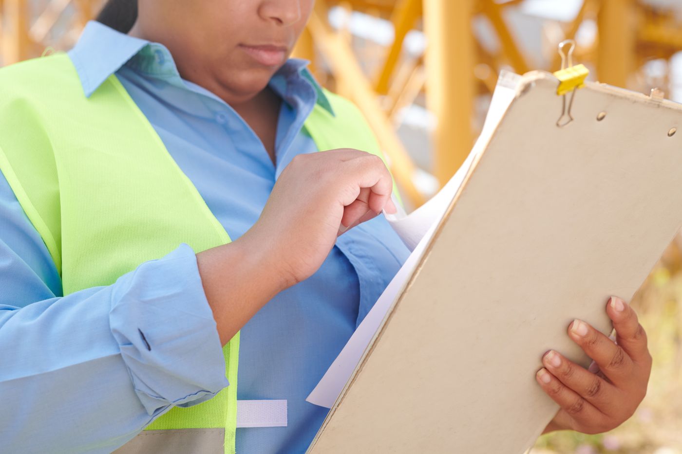 A worker in a high-visibility vest pages through a clipboard on site.