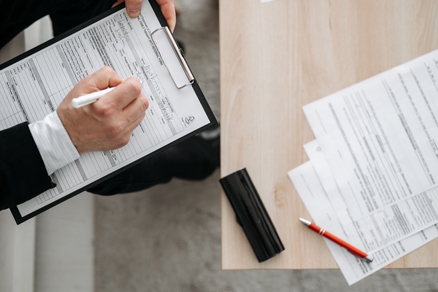 High-angle view of a person filling out forms on a clipboard, emphasizing paperwork and documentation.