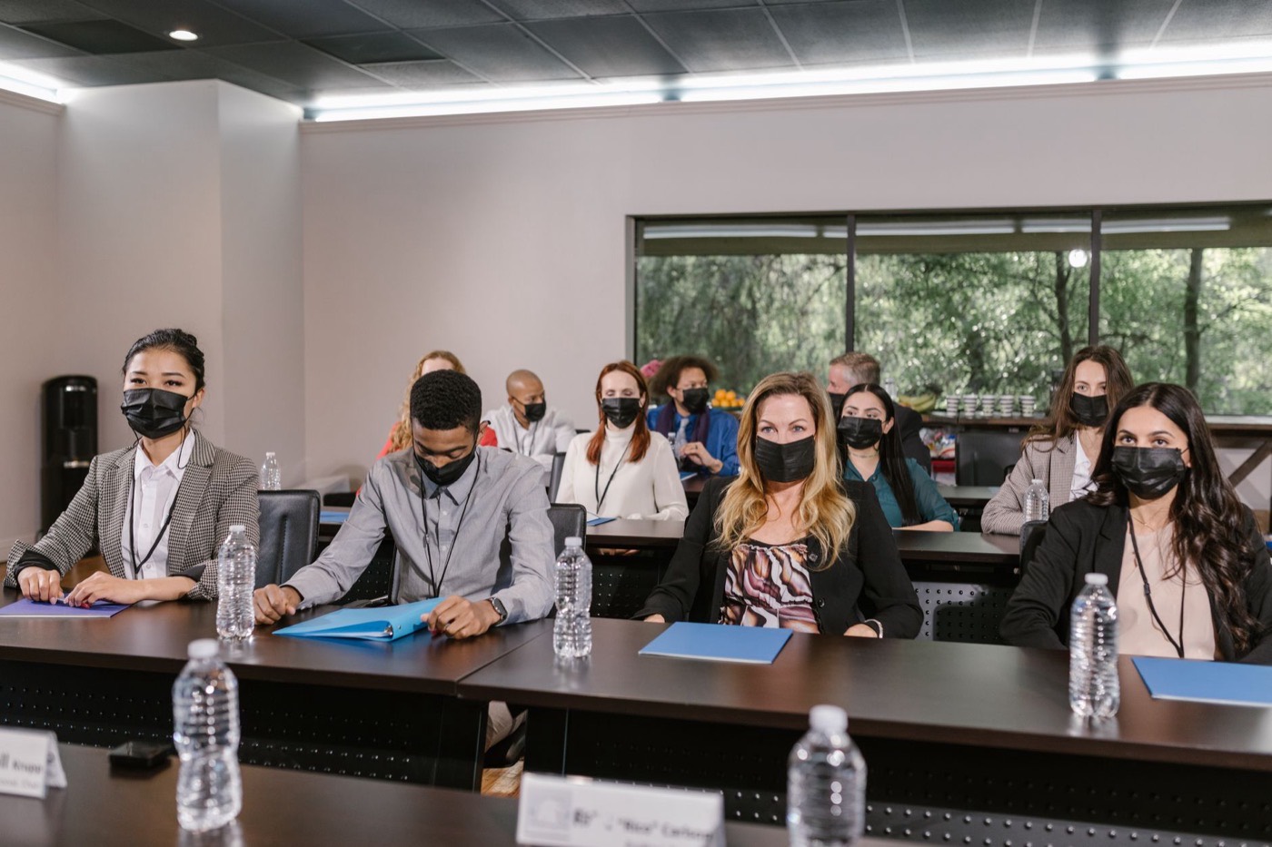 A group of masked professionals in a business meeting setting, maintaining social distance.
