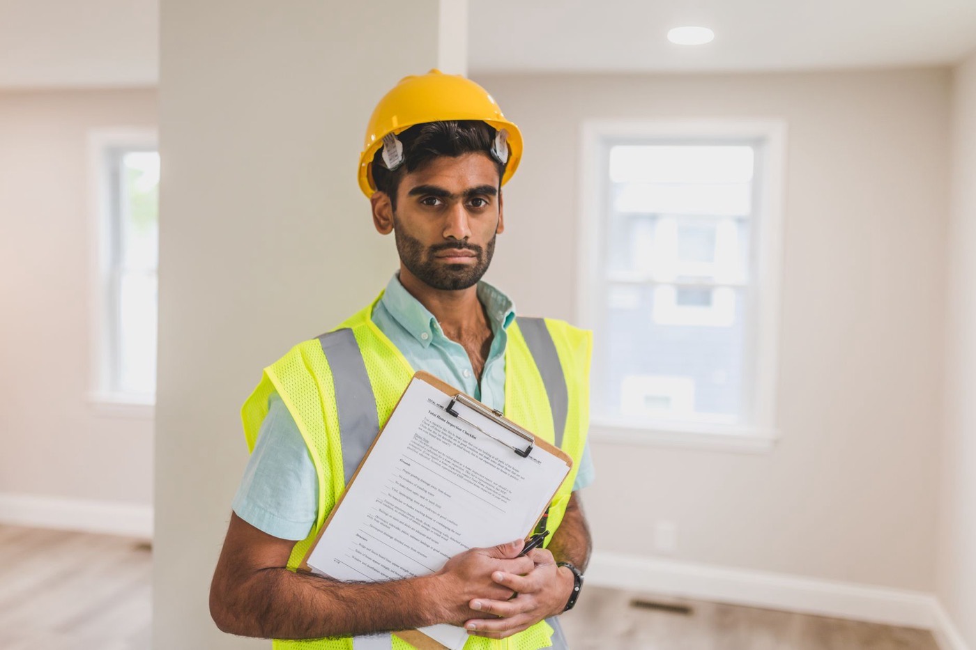 South Asian construction worker wearing safety gear and holding a clipboard indoors.